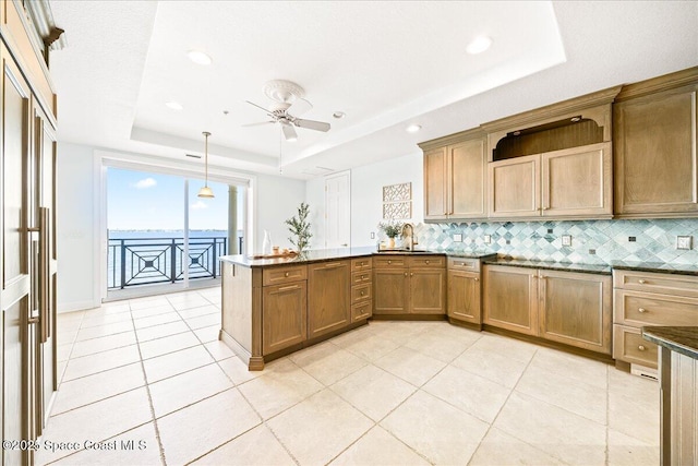 kitchen featuring pendant lighting, a raised ceiling, brown cabinetry, and decorative backsplash