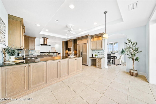 kitchen with paneled built in fridge, island exhaust hood, a tray ceiling, and decorative light fixtures