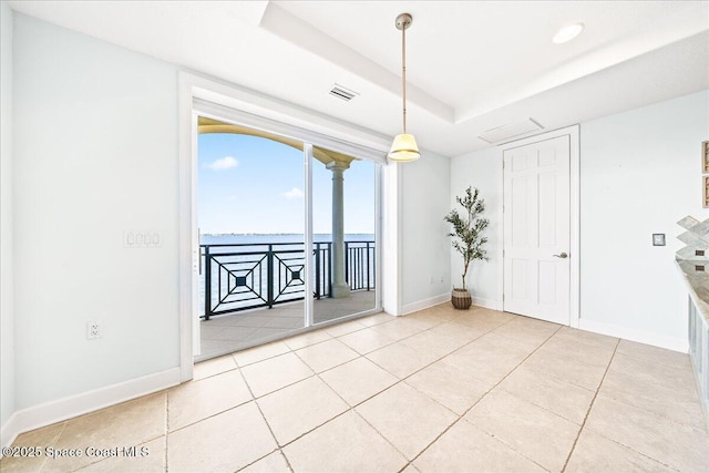 empty room with light tile patterned floors, a raised ceiling, visible vents, a water view, and baseboards