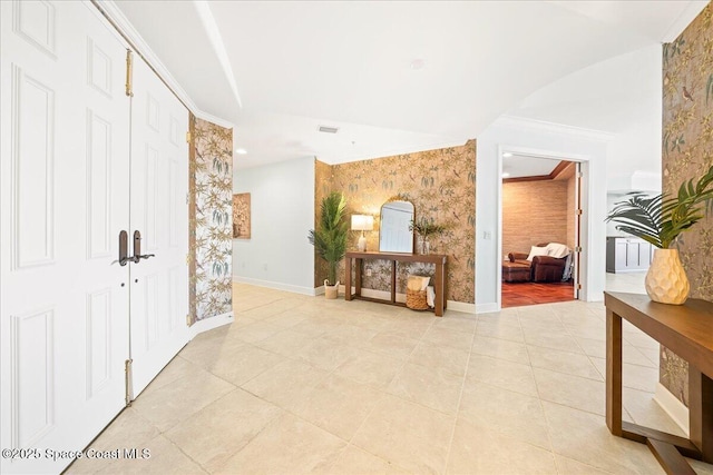 hall with crown molding, wallpapered walls, light tile patterned flooring, and baseboards