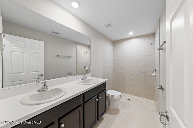 bathroom featuring toilet, tile patterned floors, tiled shower, and vanity