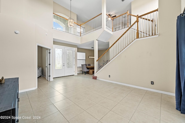 foyer entrance featuring light tile patterned flooring, a towering ceiling, a notable chandelier, and french doors