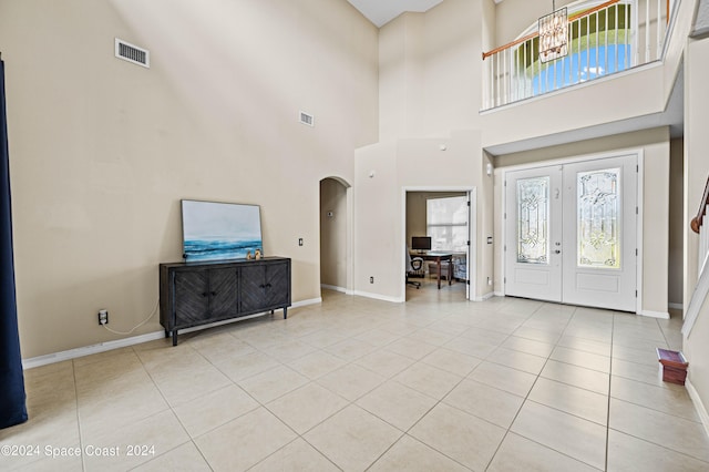 entryway with a towering ceiling, a notable chandelier, french doors, and light tile patterned floors