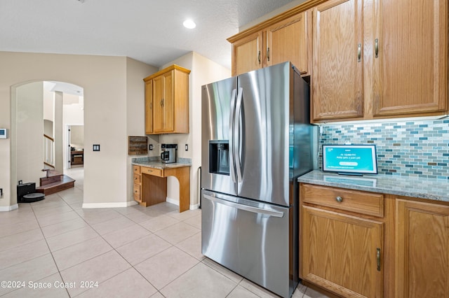 kitchen with backsplash, stainless steel fridge, light stone countertops, and light tile patterned floors