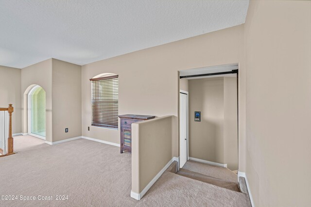 hallway featuring light colored carpet and a textured ceiling