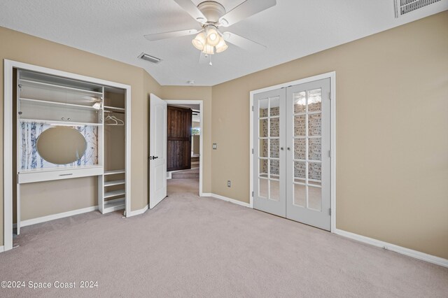 unfurnished bedroom featuring french doors, a textured ceiling, ceiling fan, a closet, and light colored carpet