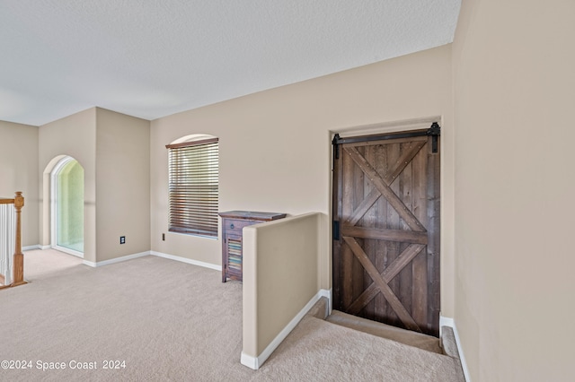 hallway with a textured ceiling, carpet floors, and a barn door