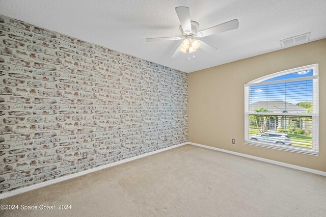 unfurnished room featuring a textured ceiling, brick wall, ceiling fan, and light colored carpet