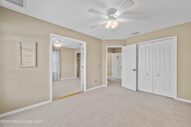 unfurnished bedroom featuring ceiling fan, a closet, a textured ceiling, and light colored carpet