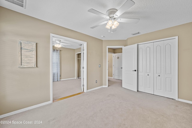 unfurnished bedroom with light colored carpet, a textured ceiling, ceiling fan, and a closet