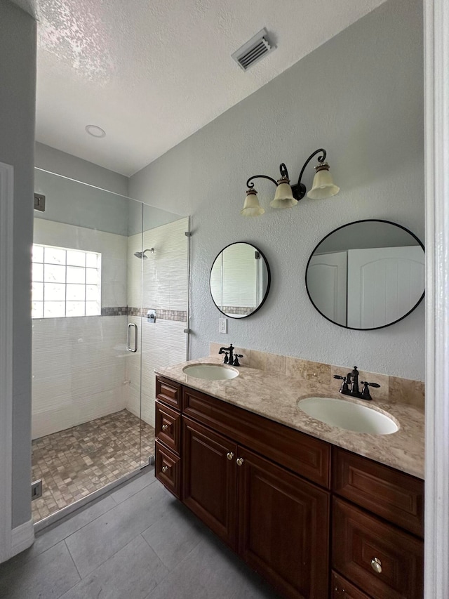 bathroom featuring a shower with door, a textured ceiling, double sink vanity, and tile patterned flooring