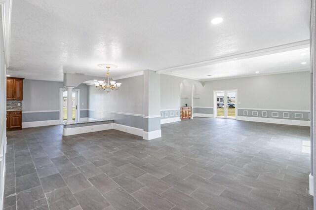 unfurnished living room with a notable chandelier, ornate columns, dark tile patterned floors, and crown molding