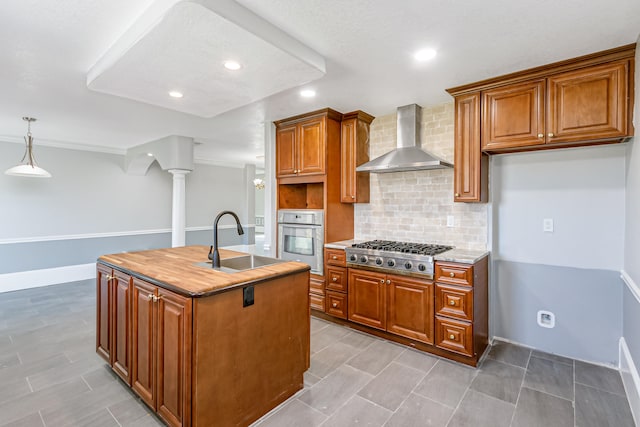 kitchen featuring appliances with stainless steel finishes, tasteful backsplash, sink, an island with sink, and wall chimney exhaust hood