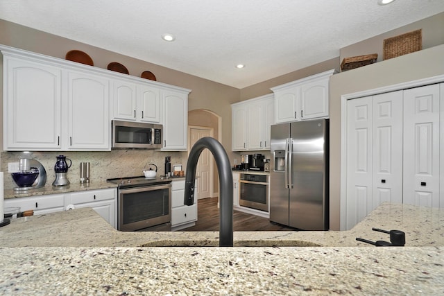 kitchen with light stone countertops, white cabinetry, stainless steel appliances, and tasteful backsplash