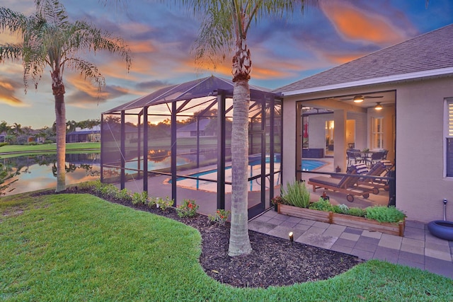 yard at dusk featuring a water view, a lanai, and a patio area