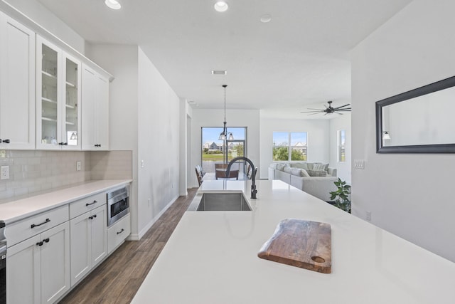 kitchen with hanging light fixtures, white cabinetry, stainless steel microwave, and sink