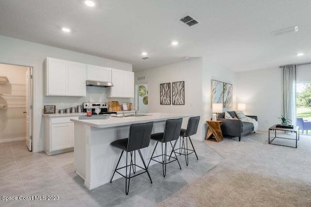 kitchen featuring a kitchen breakfast bar, stainless steel range, a center island with sink, and white cabinets