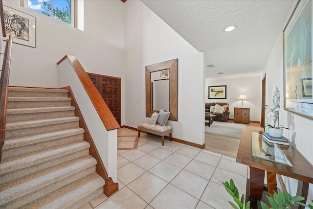 foyer featuring a towering ceiling, a textured ceiling, and light tile patterned flooring