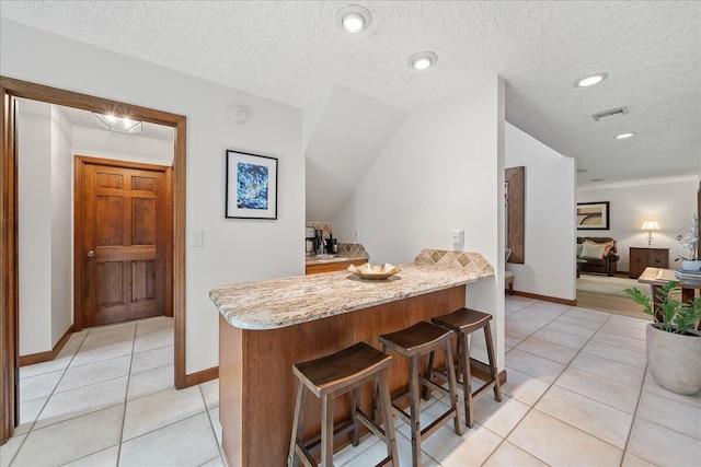 kitchen featuring kitchen peninsula, light tile patterned floors, a kitchen bar, and light stone counters