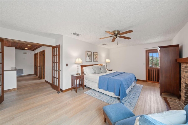 bedroom with ceiling fan, light hardwood / wood-style floors, a textured ceiling, and a brick fireplace