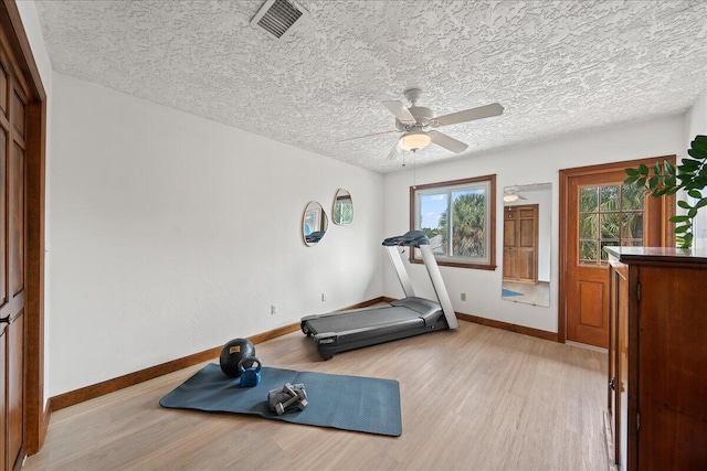 workout room with ceiling fan, light hardwood / wood-style flooring, and a textured ceiling