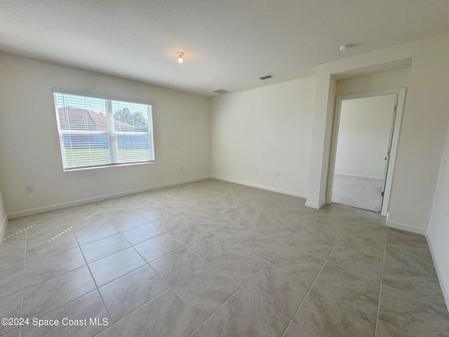 empty room with light tile patterned flooring and a textured ceiling