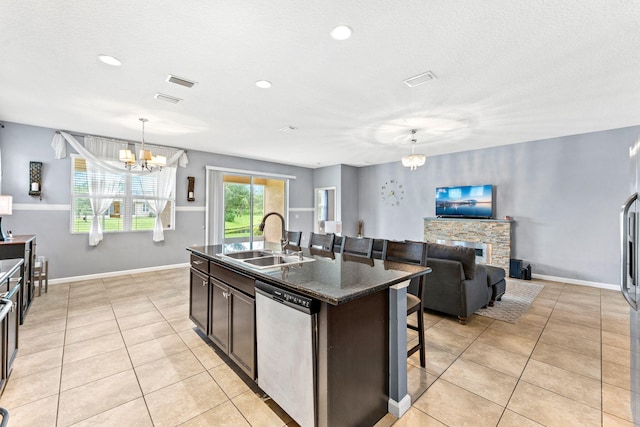 kitchen with an island with sink, hanging light fixtures, sink, stainless steel dishwasher, and a fireplace