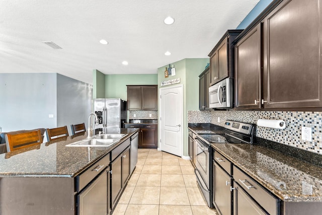 kitchen featuring appliances with stainless steel finishes, sink, dark brown cabinetry, light tile patterned floors, and a center island with sink