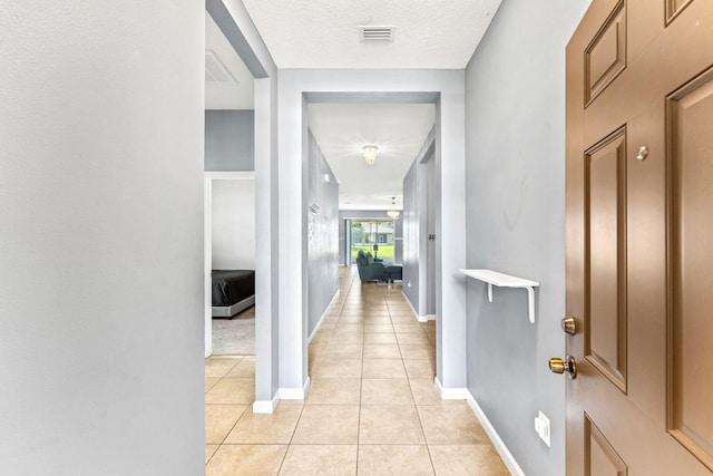 hall with a textured ceiling and light tile patterned floors