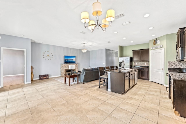 kitchen with a notable chandelier, dark brown cabinets, a center island with sink, and a breakfast bar area