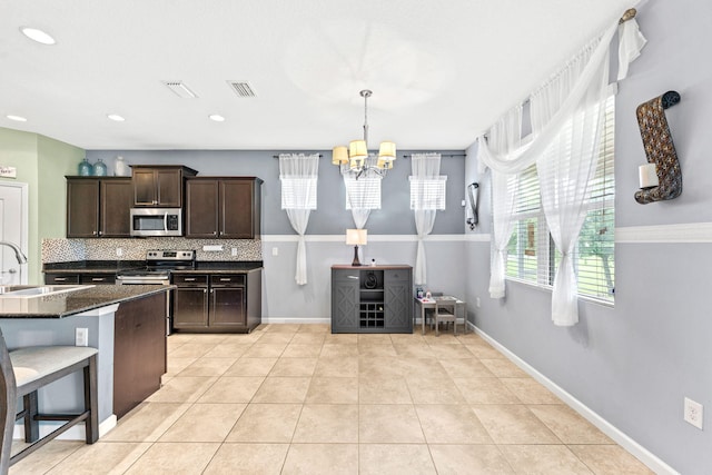 kitchen featuring decorative backsplash, appliances with stainless steel finishes, a kitchen breakfast bar, dark stone counters, and dark brown cabinetry