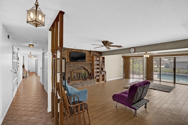 tiled living room with a textured ceiling, a fireplace, and ceiling fan with notable chandelier