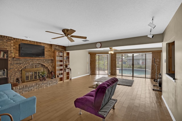 living room featuring a fireplace, wood-type flooring, a textured ceiling, and ceiling fan