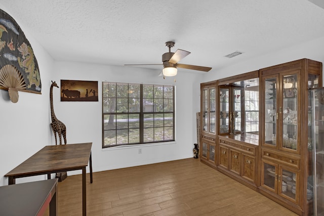 dining space featuring wood-type flooring, ceiling fan, and a textured ceiling