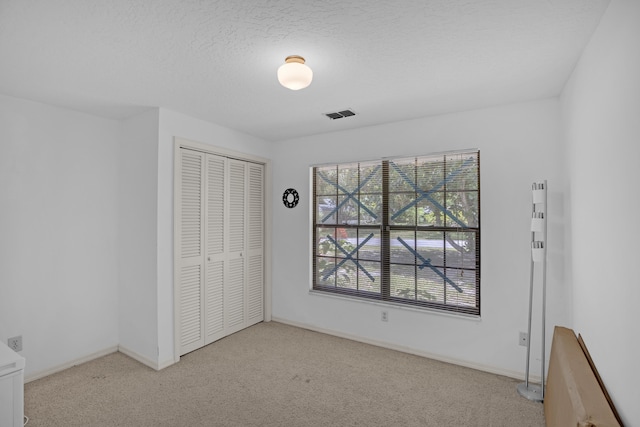 unfurnished bedroom featuring a closet, light carpet, and a textured ceiling