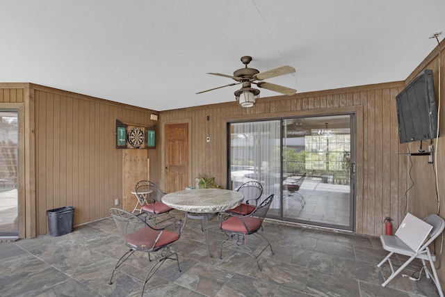 unfurnished dining area with ceiling fan and wood walls