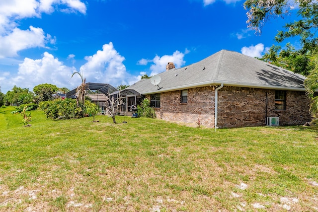 rear view of property featuring a lanai, a lawn, and ac unit