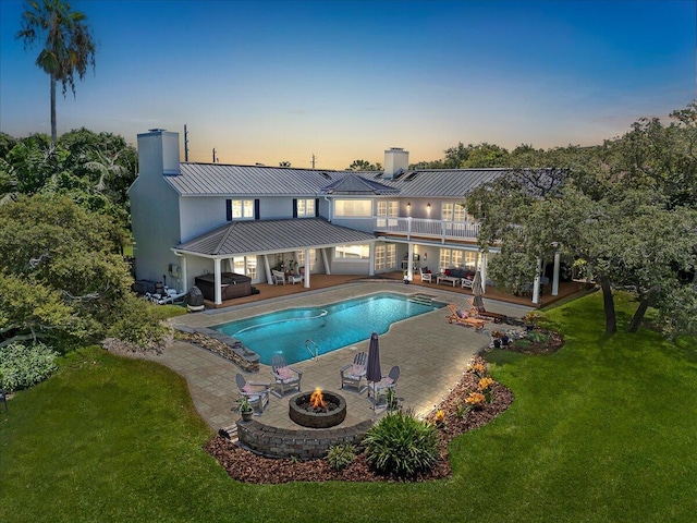 pool at dusk with a yard, a patio, and an outdoor living space with a fire pit