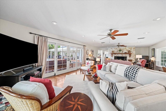 living room featuring a fireplace, ceiling fan, french doors, and light hardwood / wood-style flooring