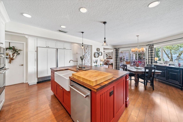 kitchen featuring dishwasher, an inviting chandelier, a center island with sink, sink, and white cabinetry