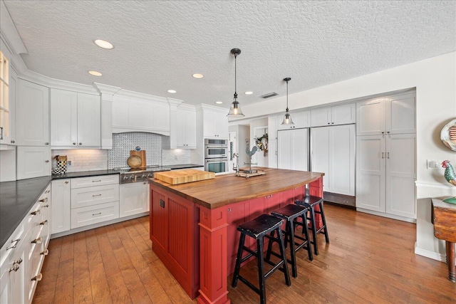 kitchen featuring butcher block counters, hanging light fixtures, backsplash, an island with sink, and a breakfast bar area