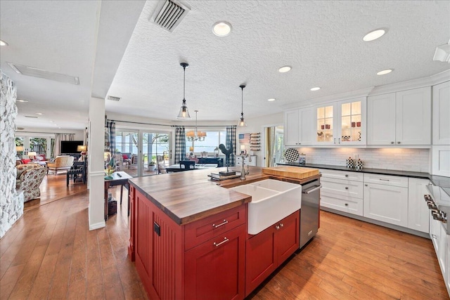 kitchen with wood counters, backsplash, stainless steel dishwasher, and a kitchen island with sink