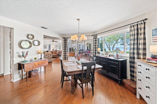 dining area featuring ceiling fan with notable chandelier, a textured ceiling, and dark hardwood / wood-style flooring