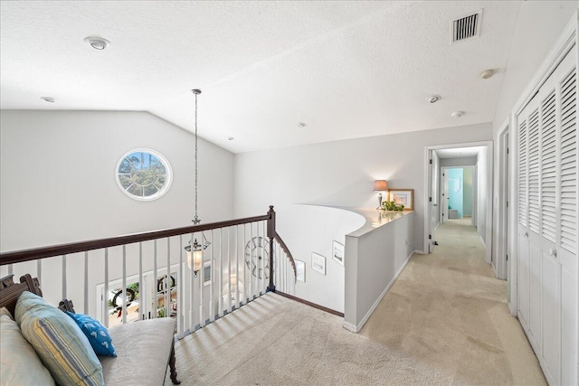 hallway featuring a textured ceiling, light colored carpet, vaulted ceiling, and a healthy amount of sunlight