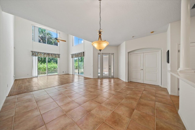 interior space featuring tile patterned flooring, ceiling fan, a towering ceiling, a textured ceiling, and decorative columns