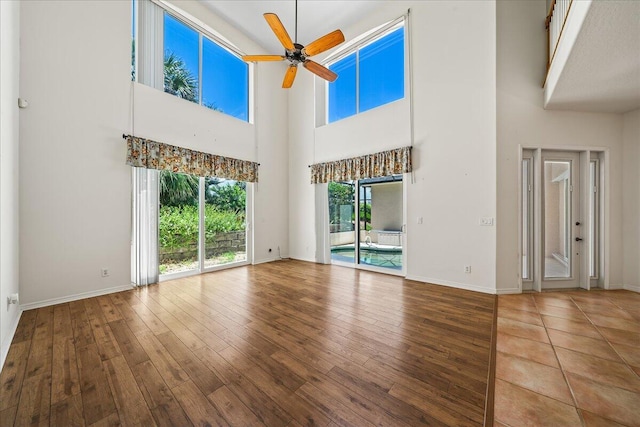 unfurnished living room with hardwood / wood-style floors, a towering ceiling, and ceiling fan