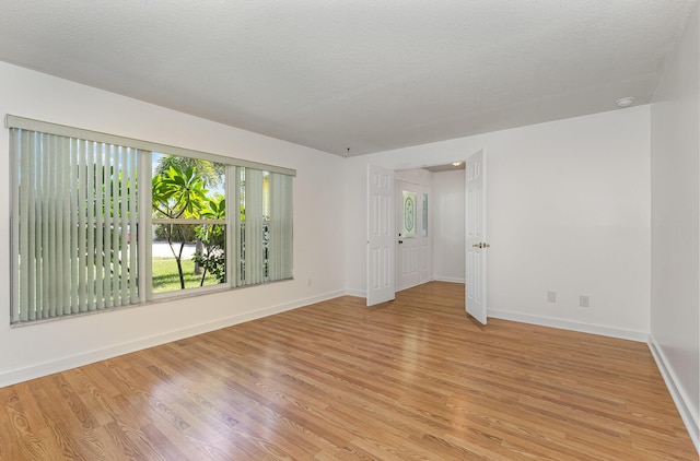 empty room with a textured ceiling and light hardwood / wood-style flooring