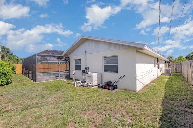 back of property with a pool, a lanai, central AC, and a lawn