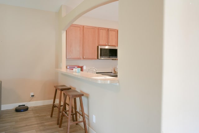 kitchen featuring light brown cabinetry, a kitchen breakfast bar, light hardwood / wood-style flooring, and kitchen peninsula