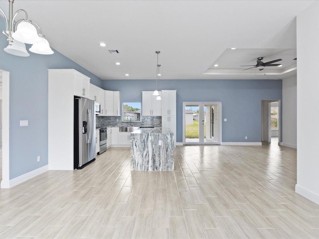 kitchen with a kitchen island, hanging light fixtures, a tray ceiling, white cabinetry, and appliances with stainless steel finishes